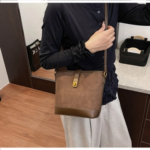 Detail of dark brown bucket bag with matte texture and golden twist lock on shoulder strap