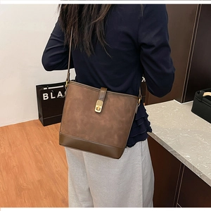 Detail of dark brown bucket bag featuring contrast textures and gold metal snap button