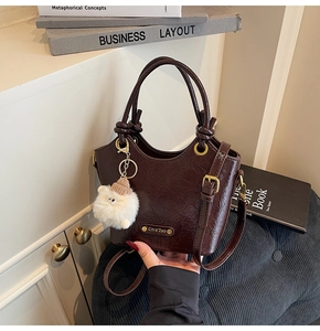 Detail of dark brown glossy bucket bag with golden buckle and plush lamb charm