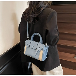 Close-up of stylish contrast color crossbody bag with dual handles and metal eyelets