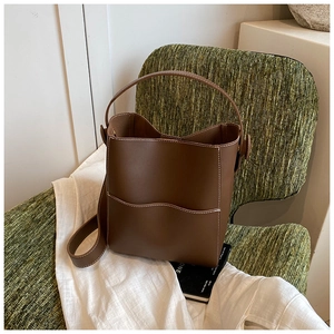 Detailed view of a brown leather bucket bag with white contrast stitching on a green chair