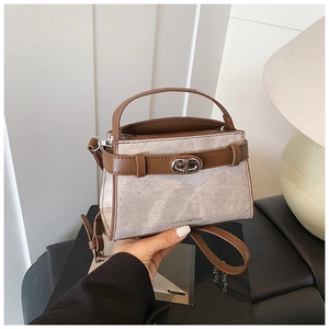 Detail view of cream textured crossbody bag with brown faux leather trim and metallic clasp