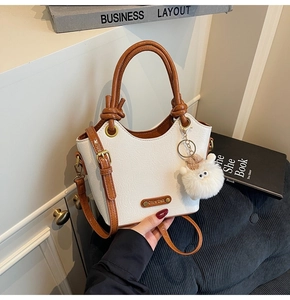 Detail of white lychee texture bucket bag with brown leather handles and plush charm