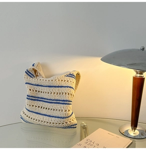 Detail of hand-knit tote bag with beige cotton texture and blue stripes on a glass table