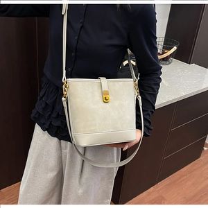 Close-up of cream leather bucket bag showing the elegant gold metal twist lock and texture