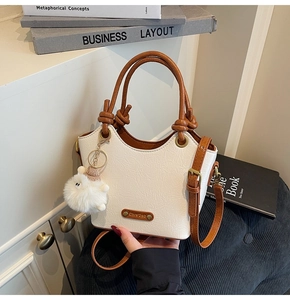 Close-up of cream pleated bucket bag with brown knotted handle and plush charm detail