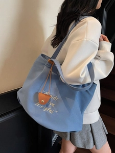 Blue canvas tote bag with white embroidery and leather charm shown as shoulder bag