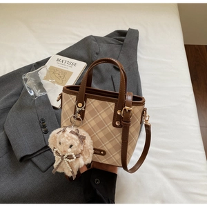 Detail of checkered tote bag with plush bunny charm, metal logo and leather strap