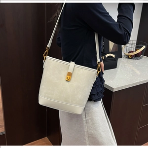 Detailed close-up of cream bucket bag with golden twist lock and textured finish