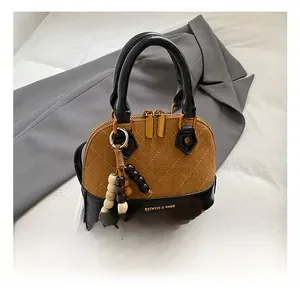 Close-up of shell handbag with brown quilted suede and black patent leather stitching