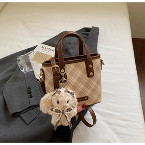 Detail of color-block plaid bucket bag with plush rabbit charm on a stylish background