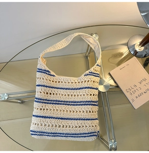 Detail view of a beige knitted bucket bag with blue stripes on a modern glass table