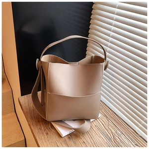 Detail view of beige leather bucket bag with contrast stitching on wooden surface