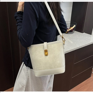 Detailed view of an off-white bucket bag with gold clasp shown on a model indoors