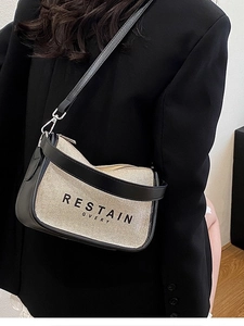 Beige canvas crossbody bag with black leather trim worn by a model in a black blazer