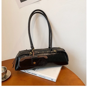 Close-up of black glossy PU leather baguette bag with detachable mini pouch on a book