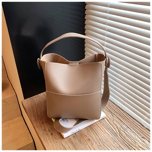 Beige bucket bag with contrast stitching on wooden surface with warm lighting