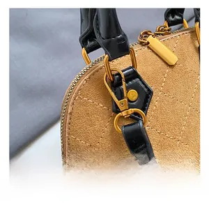 Detail of brown quilted suede shell bag with golden metal hooks and black handle