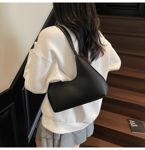 Detail view of black pebble leather crescent shoulder bag worn on a model's arm