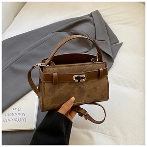 Close-up of vintage brown leather bucket bag with golden CD metal lock on a white bed