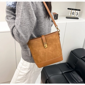 Close-up of brown bucket bag showing mixed texture materials and gold metal buckle