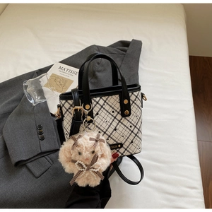 Detail of checkered tote bag with plush rabbit charm and gold brand plate