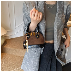 Detail of shell handbag in brown suede and black patent leather with golden hardware