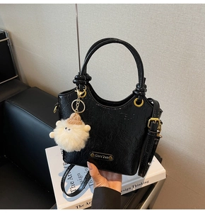 Detail of black glossy bucket bag with metal logo, double handles and plush toy charm
