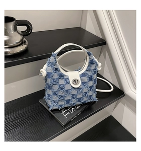 Detail of blue checkerboard denim bucket bag with frayed edges and silver turn-lock