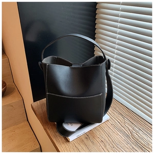 Detail of black leather bucket bag featuring white contrast stitching and wide top handle