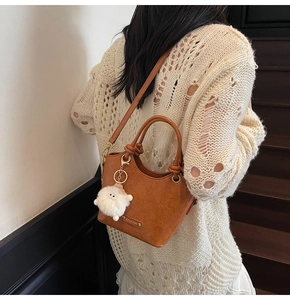 Detail of caramel vintage handbag with plush monster charm and knotted round handles