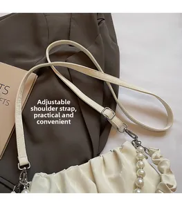 Détail de la bandoulière réglable et chaîne perlée sur un sac plissé blanc cassé