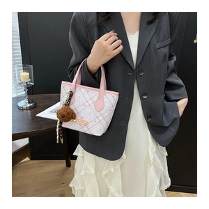 Pink plaid bucket bag with cute teddy bear charm held by model in city style
