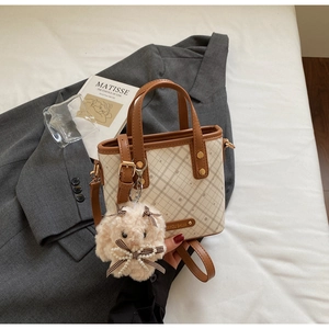 Detail of a chic cream checkered bucket bag with a brown handle and plush rabbit charm