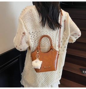 Close-up of caramel textured leather bucket bag with round handles and plush charm