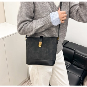 Detail of minimalist black bucket bag with gold clasp shown on a model in a modern room
