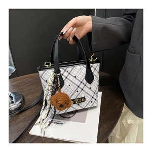 Detail of checkered bucket bag with black handles and a cute brown teddy bear pendant