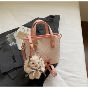 Detail of pink plaid bucket bag with plush rabbit pendant on gray suit jacket