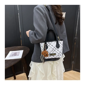 Detailed view of white checkered bucket bag featuring gold metal plaque and plush bear charm