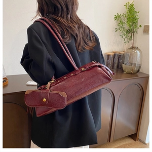 Close-up of a burgundy cylindrical shoulder bag with a matching small coin pouch detail