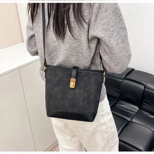 Detail of a black bucket bag featuring textured leather and a gold vintage twist-lock clasp