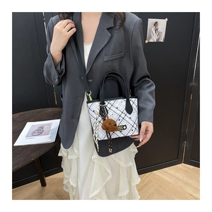 Detail of white checkered tote bag with black handles and brown teddy bear charm