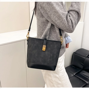 Detail view of the black bucket bag's gold metal clasp and textured leather material