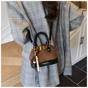 Detail of shell-shaped crossbody bag featuring brown suede and black patent leather trim