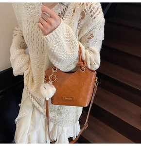 Detail of caramel leather bucket bag with glossy texture and white plush charm accessory