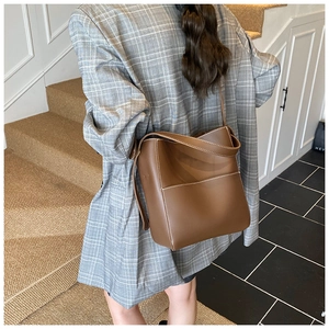 Detail of brown matte leather bucket bag featuring white contrast stitching and side pocket