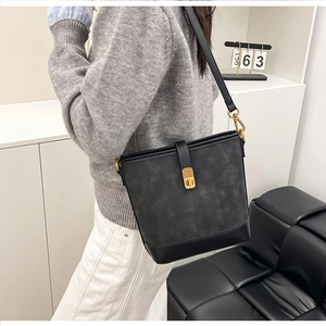 Detail of a vintage-style bucket bag with gold lock and textured leather shown on shoulder
