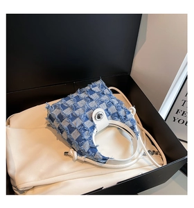Detail of blue checkerboard denim bucket bag with frayed edges and silver twist lock