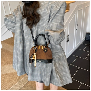 Detail of a brown suede and black patent leather shell bag with gold hardware and beaded charm
