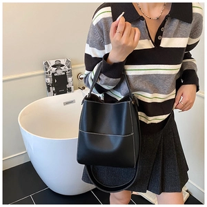 Detail of black bucket bag with white contrast stitching and front pocket on shoulder strap
